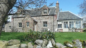 A stone house with a large glass conservatory, a stone chimney, and a well-maintained lawn.
