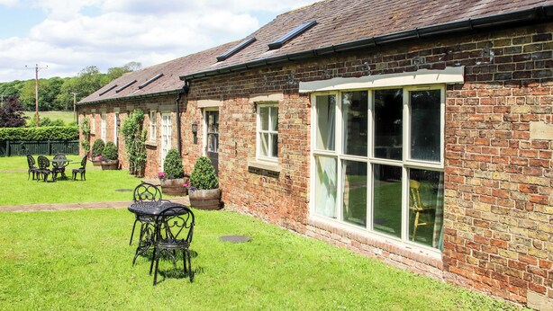 A brick building with large windows and a garden area with outdoor seating.
