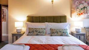 A neatly made bed with a green upholstered headboard, white bedding, and floral-patterned pillows. There are two bedside lamps on matching nightstands.