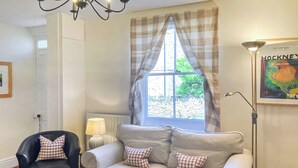 A living room with a sofa, a chair, a lamp, a window with curtains, and a framed picture on the wall.