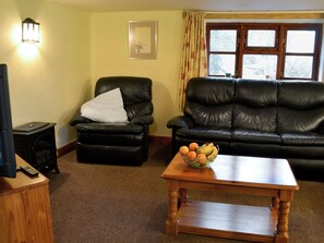 A living room with a black leather sofa, a black leather armchair, a wooden coffee table, and a small table with a fruit bowl. - 3 bedroom accommodation in Dunterton, near Tavistock (Dunterton, near Tavistock)