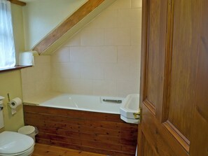 A bathroom with a wooden floor, white tiles, a bathtub, and a toilet.