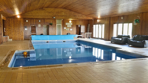Ein Hallenbad mit gefliestem Boden, Holzwänden und einer Decke mit Holzbalken.