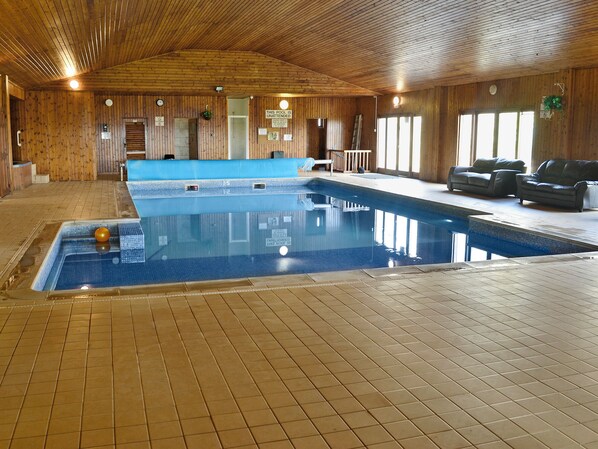 An indoor swimming pool with tiled flooring, wooden walls, and a ceiling with wooden beams.