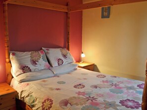 Une chambre à coucher avec un lit à baldaquin, une literie à motifs floraux, une lampe de chevet et une table de chevet avec des tiroirs.