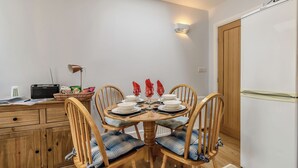 Un coin repas avec une table dressée pour deux personnes, des chaises en bois avec des coussins bleus, une radio et un panier rempli de collations.