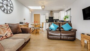 Un salon moderne avec un canapé en cuir marron, un divan à motifs et un coin repas doté de chaises en bois.