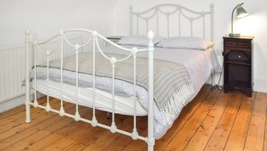 Un lit à baldaquin en métal blanc, avec une couette et des oreillers à motifs gris, une table de chevet avec une lampe et un plancher en bois.
