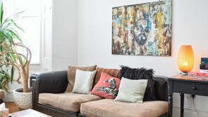 Un salon avec un canapé en cuir noir, une table basse en bois, une plante en pot et un tableau abstrait aux couleurs vives accroché au mur.