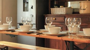 Une table à manger dressée avec des bols blancs et des verres à vin, un distributeur d’eau et un récipient à pain en arrière-plan.
