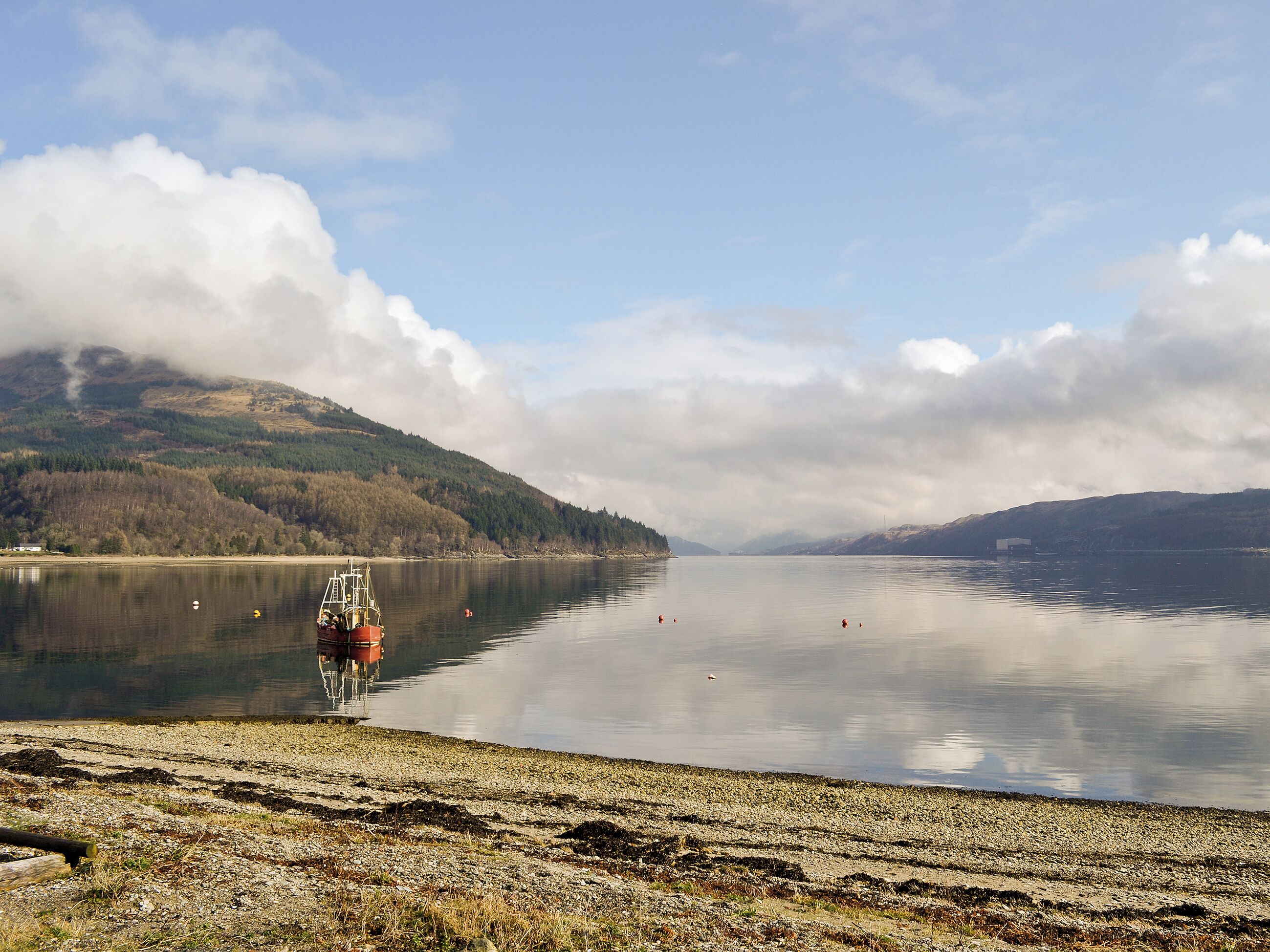 A calm lake with a boat docked on the shore, surrounded by mountains and a clear sky.