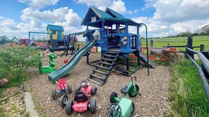 Une aire de jeux avec un toboggan, des balançoires et une cabane.