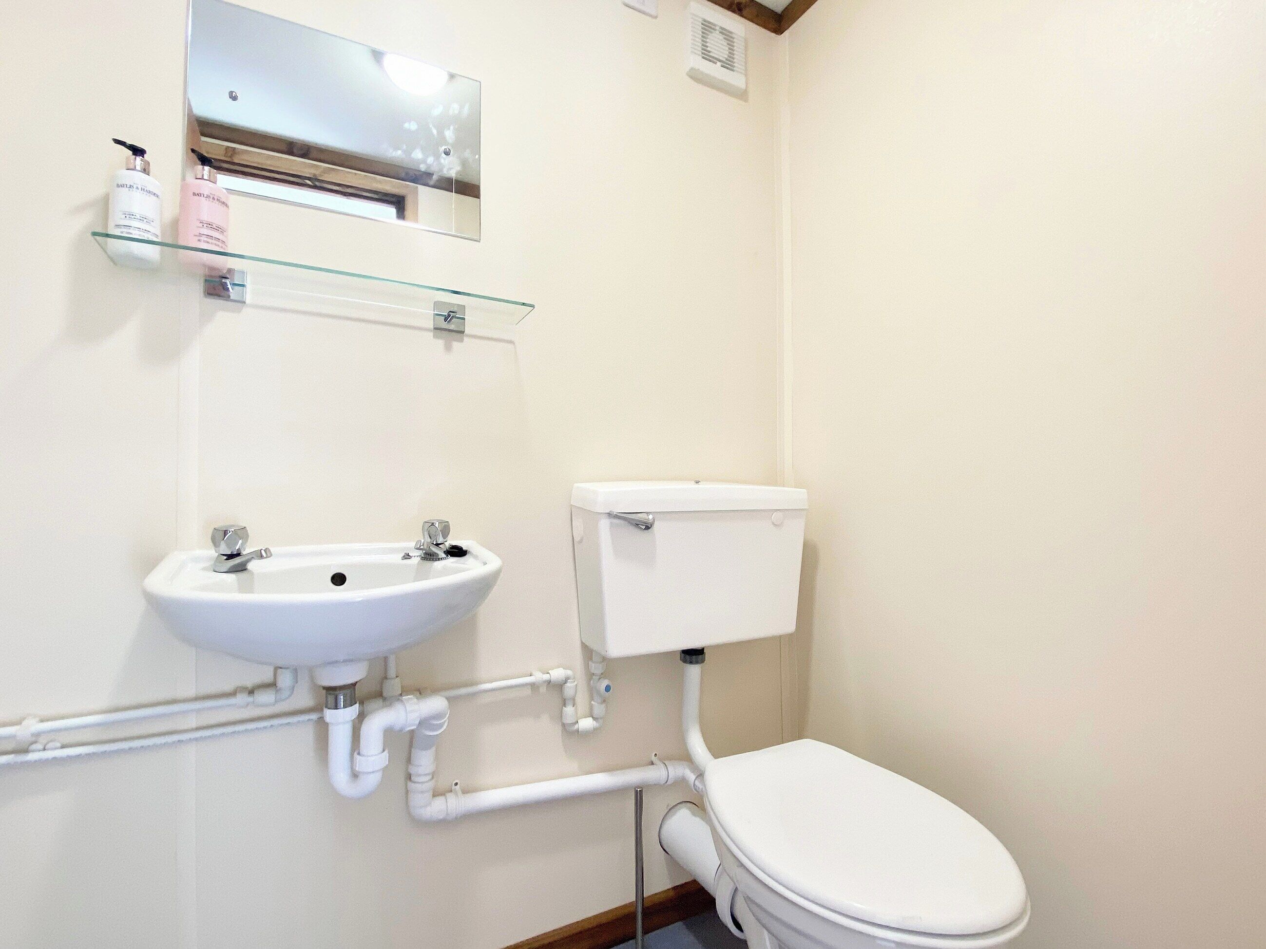 Une salle de bain avec un lavabo blanc, des toilettes et une étagère en verre au-dessus du lavabo.