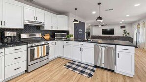 A modern kitchen with white cabinets, stainless steel appliances, and a black and white checkered rug. - Hot Tub | Game Room | Sleeps 10 & Pets (Cedar Park)