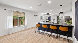 A modern kitchen with a central island, bar stools, and a large window with curtains. - Hot Tub | Game Room | Sleeps 10 & Pets (Cedar Park)