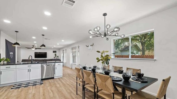 A modern kitchen with white cabinets, a central island, and a dining area with a black table and beige chairs. - Hot Tub | Game Room | Sleeps 10 & Pets (Cedar Park)