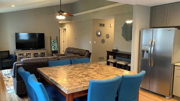 A modern kitchen with a granite countertop, stainless steel refrigerator, and a dining area with blue chairs. - Newly renovated 1400 Square Foot 3 Bedroom Home. (Indianapolis,)
