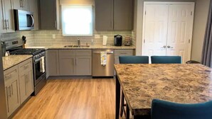 A modern kitchen with grey cabinets, a stainless steel refrigerator, a microwave, a stove, a sink, and a dining area with a table and chairs. - Newly renovated 1400 Square Foot 3 Bedroom Home. (Indianapolis,)