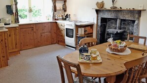 A cozy kitchen with wooden cabinets, a stove, and a dining table set for a meal. - A rural, detached cottage within the historic grounds of the Bargaly Estate. (Palnure near Newton Stewart)