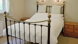 A neatly made bed with a metal frame and white bedding, two bedside tables, and wall-mounted light fixtures. - A rural, detached cottage within the historic grounds of the Bargaly Estate. (Palnure near Newton Stewart)