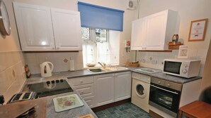 Una cucina compatta con mobili bianchi, un forno a microonde, una lavatrice e un tostapane.