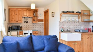 A living room with a blue sofa, wooden cabinets, a kitchen with a microwave, stove, and various utensils. - 1 bedroom accommodation in Windermere (Windermere)