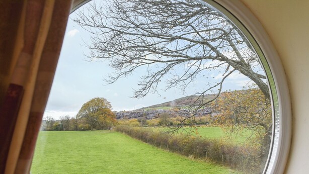A view through a window of a green field, a tree, and a hill with buildings in the distance. - 1 bedroom accommodation in Windermere (Windermere)