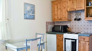 A compact kitchen with wooden cabinets, a microwave, a stove, and a glass dining table with chairs. - 1 bedroom accommodation in Windermere (Windermere)