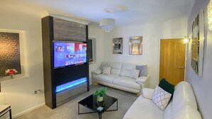 Una sala de estar moderna con un televisor de pantalla plana, sofás blancos, una mesa de centro y una araña.