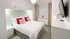 Un dormitorio con cama, mesita de noche, cómoda, espejo y ventana con cortinas.