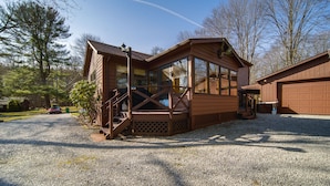 A wooden cabin with a porch, large windows, and a gravel driveway. - Charming Pymatuning Lake House Near Park & Beach (Andover)