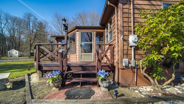 A wooden house with a porch, a small garden with potted plants, and a clear sky. - Charming Pymatuning Lake House Near Park & Beach (Andover)