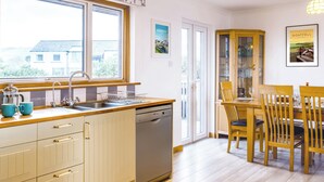 A kitchen with a sink, dishwasher, and dining area with chairs and a table.