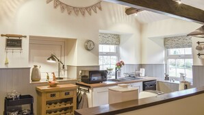 A kitchen with wooden beams, a clock, a kettle, a microwave, and a wine rack.