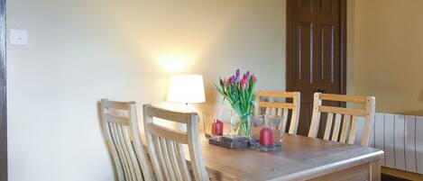 A wooden dining table with chairs, a lamp, and a vase with flowers.