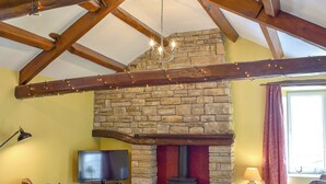 A cozy living room with a stone fireplace, wooden beams, a flat-screen TV, and comfortable seating.