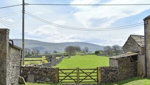 A rural landscape with a stone gate, stone walls, and a clear sky.