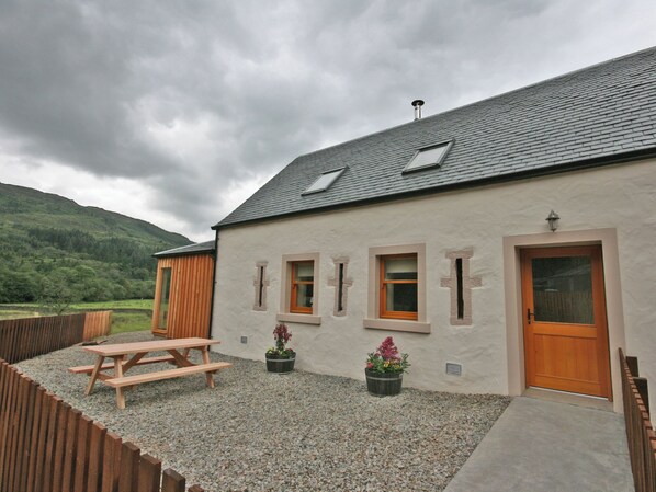 Ein Haus mit schrägem Dach, mehreren Fenstern, einer Holztür und einem Picknicktisch.