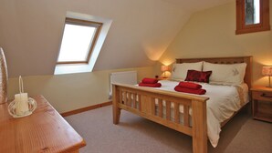 Ein Schlafzimmer mit schrägen Wänden, einem Bett mit roten Handtüchern, einem hölzernen Nachttisch und einem Fenster.