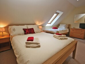 Ein Schlafzimmer mit zwei Betten, einer hölzernen Bank, einem Nachttisch, einem Schminktisch und einem Dachfenster.