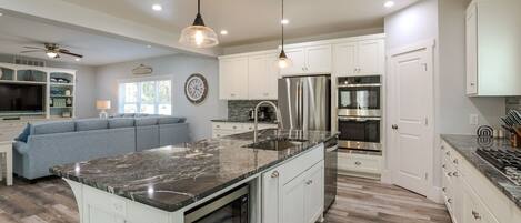 A modern kitchen with white cabinetry, a large island with a granite countertop, stainless steel appliances, and pendant lighting.