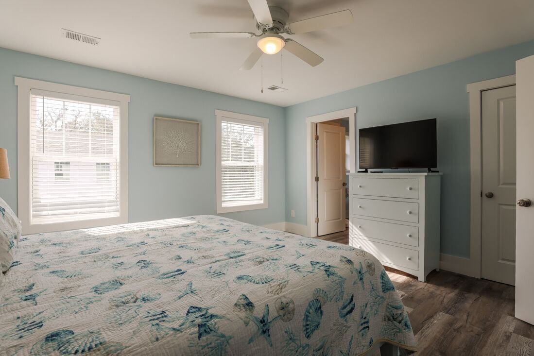 Une chambre à coucher avec un lit, un téléviseur posé sur une commode et un ventilateur de plafond.