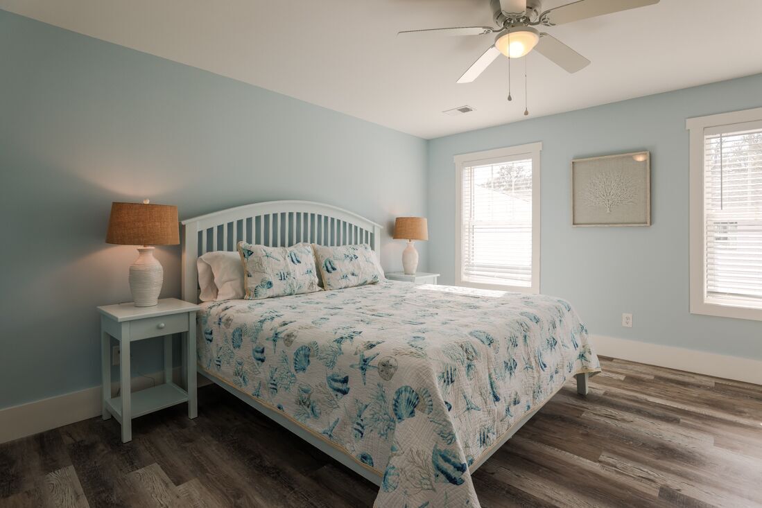 A bedroom with a bed, two nightstands, a ceiling fan, and a window with blinds.