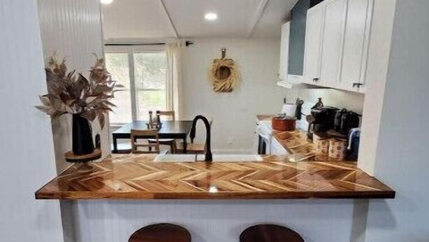Een keuken met een houten aanrecht, twee krukken en een eettafel met stoelen.