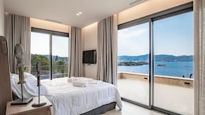 Ein modernes Hotelzimmer mit einem großen Bett, einem Flachbildfernseher und einem Balkon mit Meerblick.