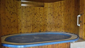 Uma área de spa com estrutura de madeira, incluindo uma banheira de hidromassagem, um painel de madeira e piso ladrilhado.