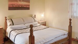 Quarto com uma cama de madeira com dossel, roupa de cama branca, mesa de cabeceira com abajur e um quadro de um pôr do sol na parede.