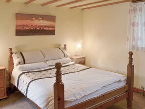 Un dormitorio con una cama de madera con dosel, ropa de cama blanca, una mesita de noche con lámpara y un cuadro de un atardecer en la pared.