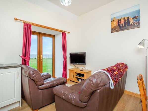A room with a brown leather sofa, a television on a wooden stand, and a painting of a coastal landscape. - 2 bedroom accommodation in Mey, near Thurso (Mey, near Thurso)