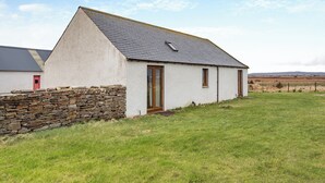 A single-story house with a sloped roof, a stone wall in front, and a grassy yard. - 2 bedroom accommodation in Mey, near Thurso (Mey, near Thurso)